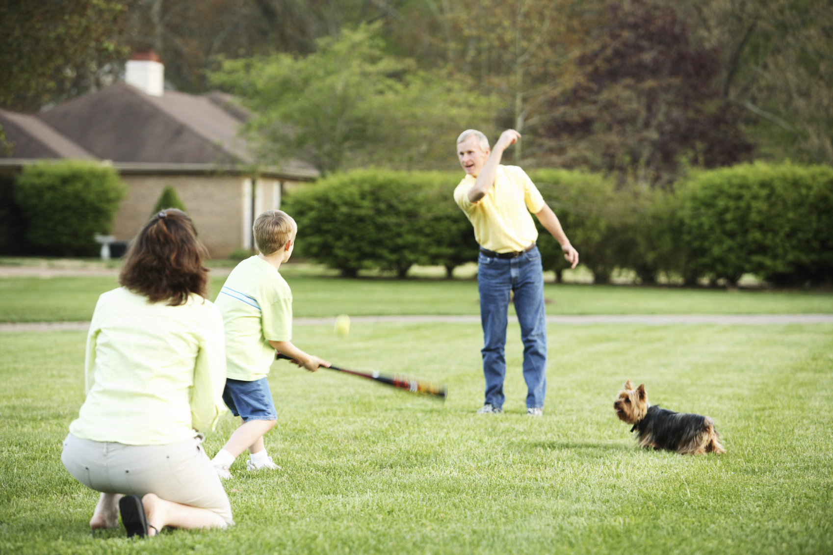 Family (father, mother, son, and pet dog) playing baseball in the yard