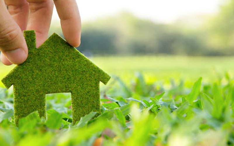A hand holding a cutout of a green house in a lawn of green grass