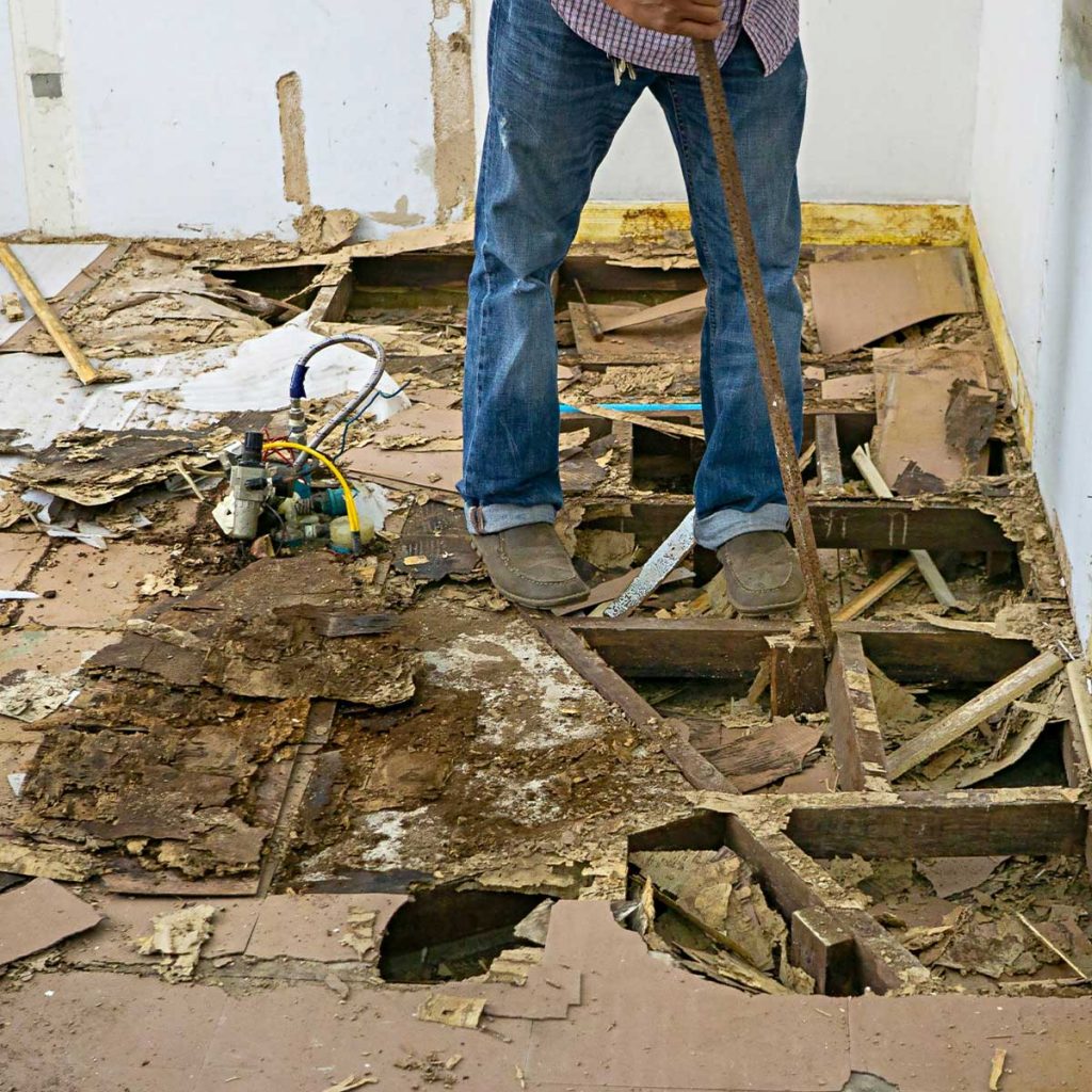 Man working to repair termite damage done to the floor of a home